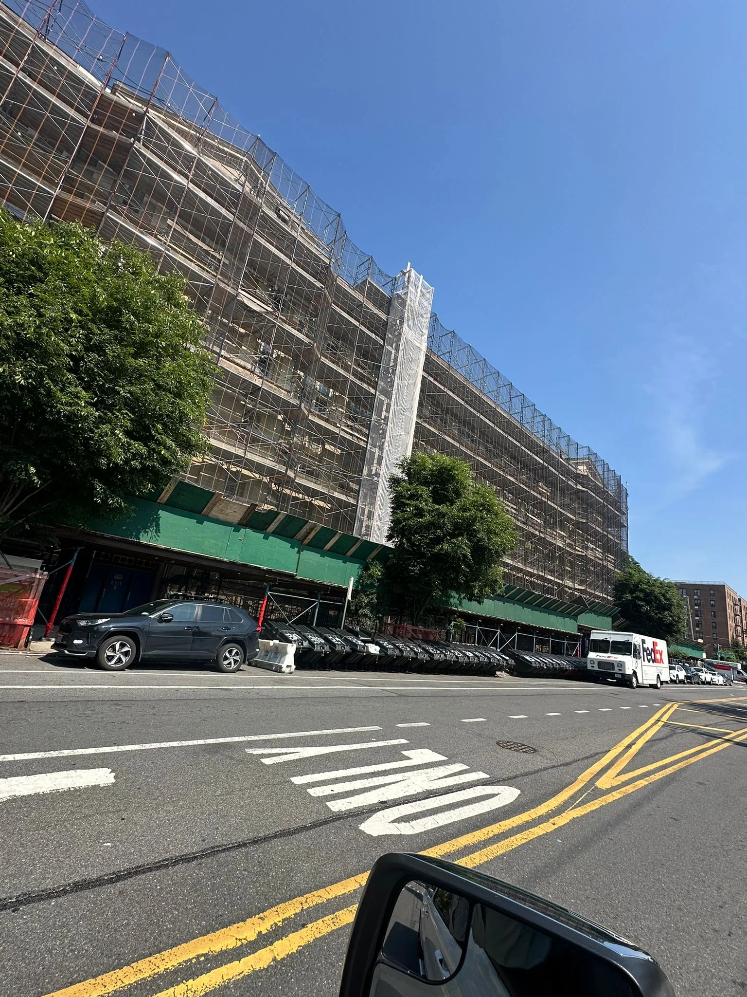 Large Bronx apartment building fully enclosed in scaffolding and sidewalk shed along a city street.